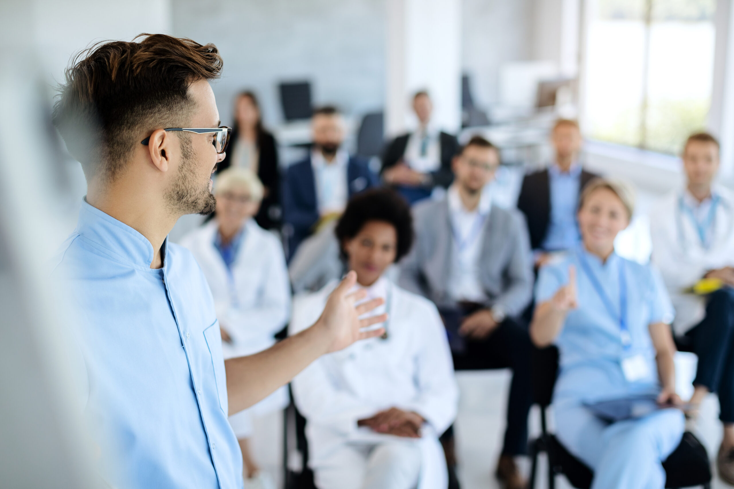 Male healthcare worker giving presentation to group of people in board room. Young doctor talking to group of his colleagues and business people during presentation in convention center.